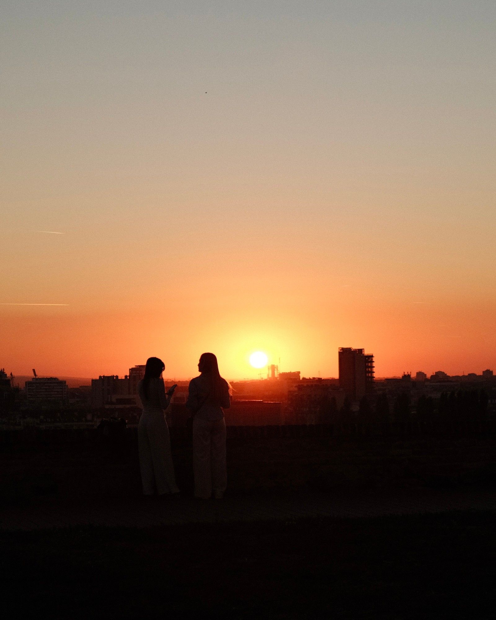 Two silhouettes watching the sun set over the city